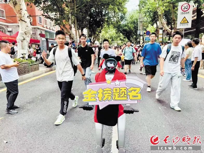 机器人“笨笨”高举“金榜题名”海报,送考生们进考场。 长沙晚报全媒体记者 李卓 摄