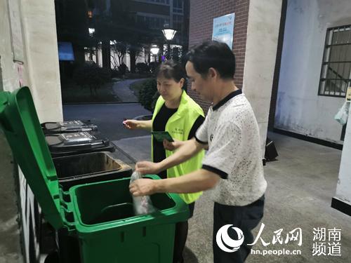 卢浮社区磊鑫嘉苑小区的“垃圾管家”在垃圾桶边指导，并为投放正确的居民盖章积分。刘丽莎供图